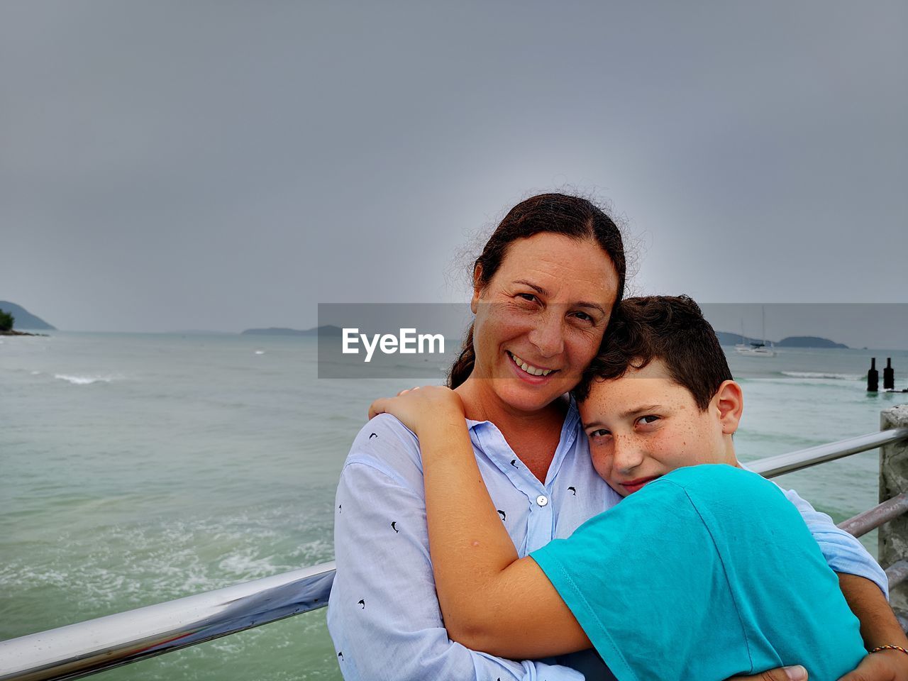 Portrait of son embracing mother against sea