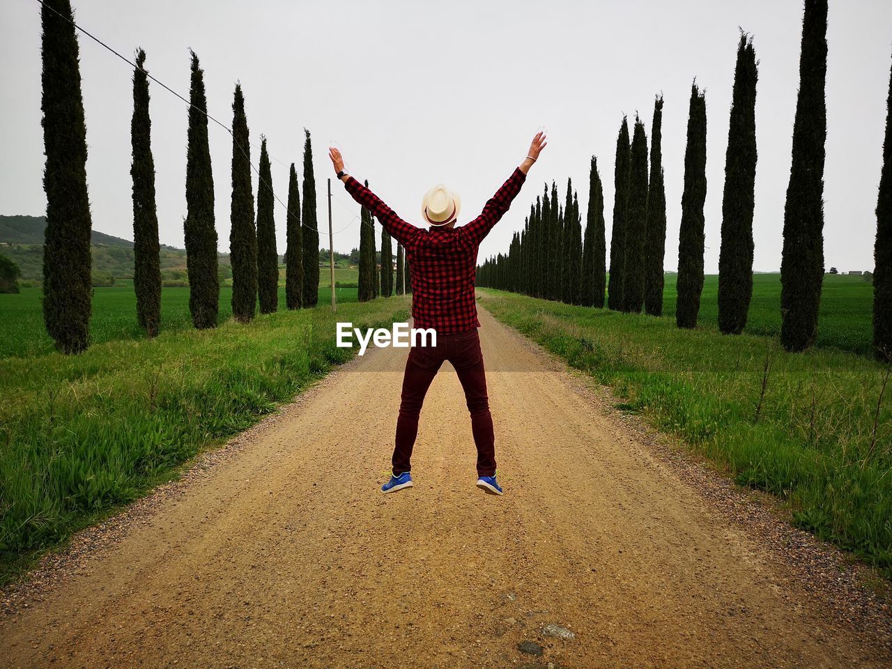 Rear view of man jumping with arms outstretched against sky