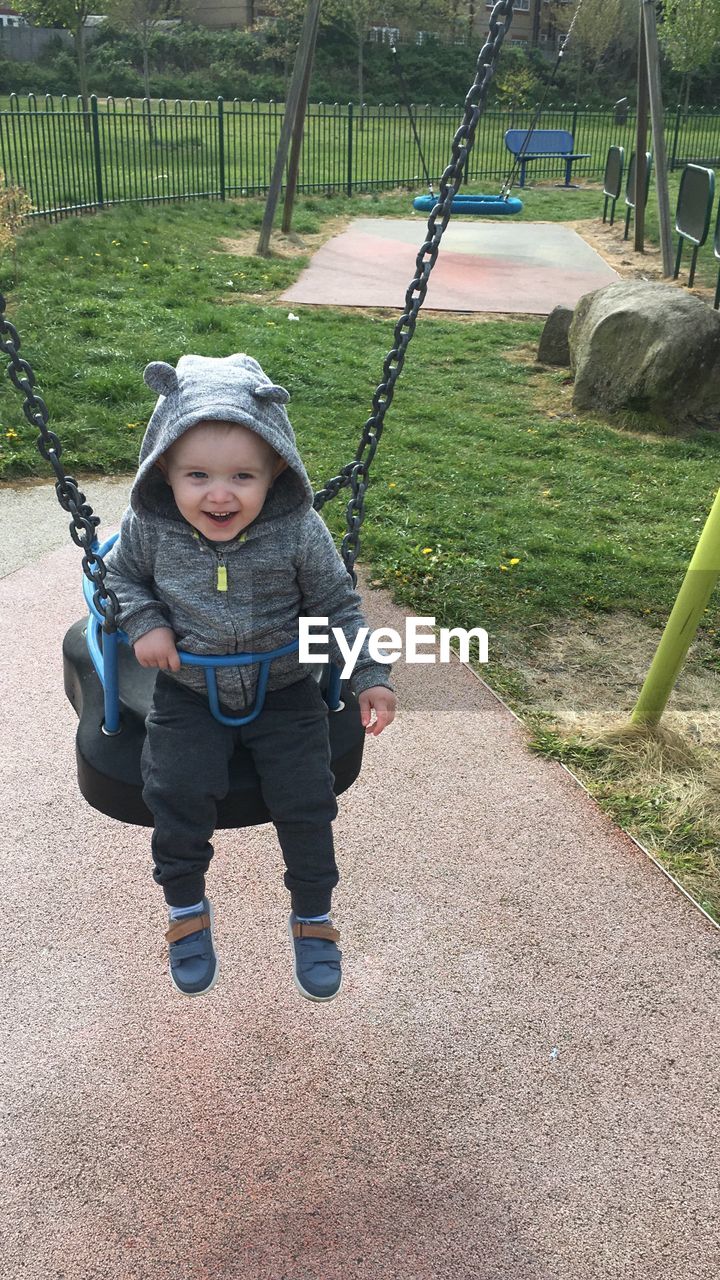 Full length of happy baby boy enjoying on swing at park
