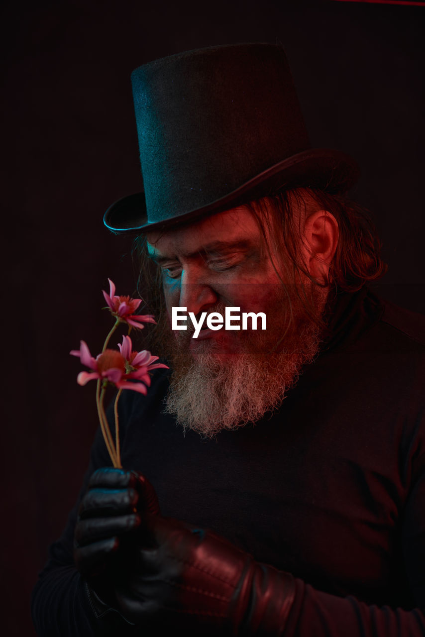 red, adult, one person, facial hair, beard, hat, men, portrait, clothing, darkness, studio shot, person, indoors, fedora, fashion accessory, senior adult, black background, emotion, dark, headshot, plant, human face, mature adult, flower, lifestyles