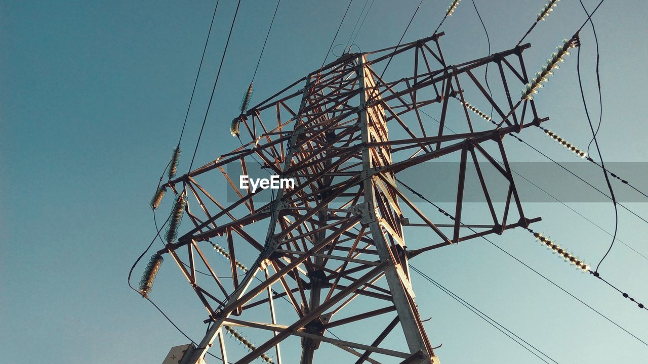 Low angle view of electricity pylon against clear blue sky