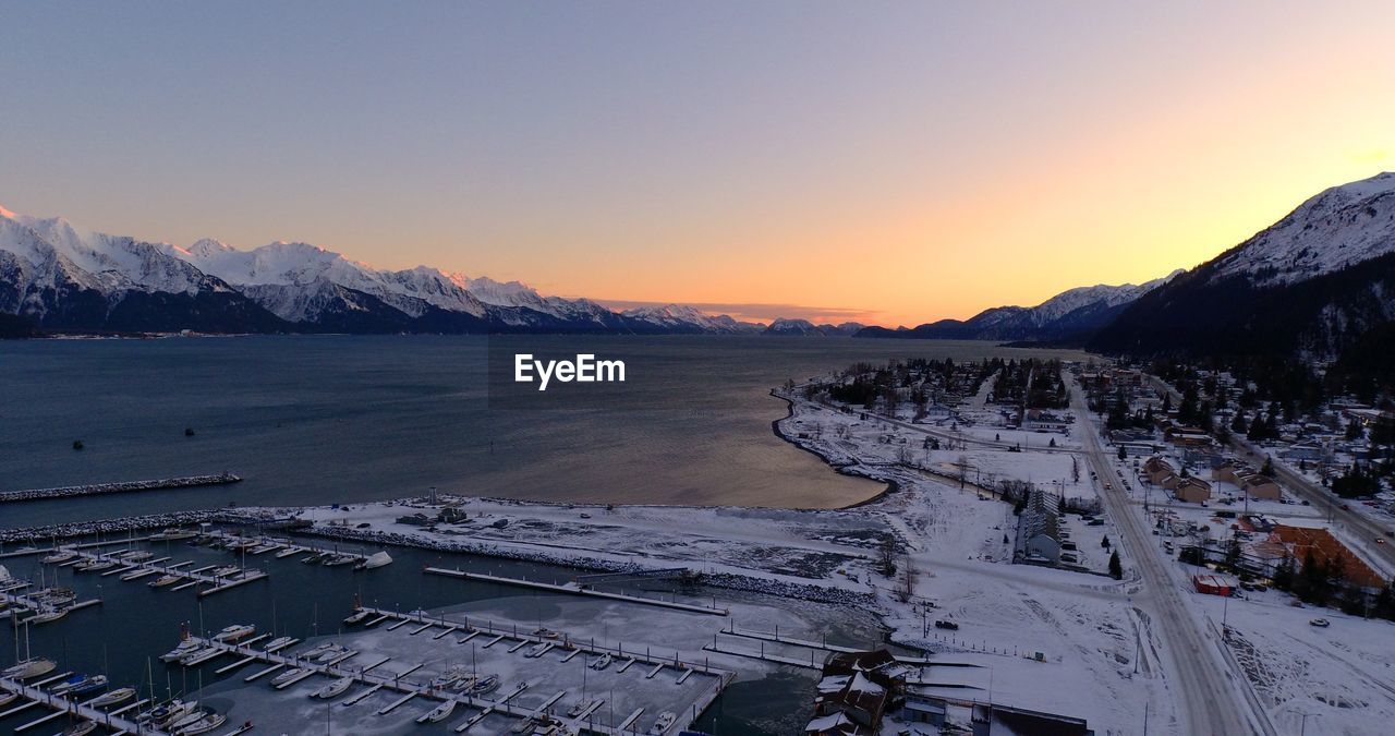Scenic view of sea by snowcapped mountains against sky during sunset