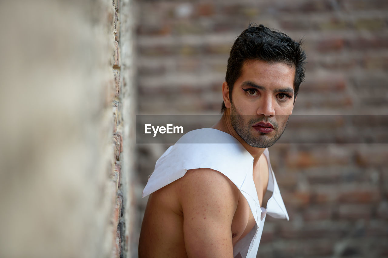 Portrait of man with make-up standing against wall