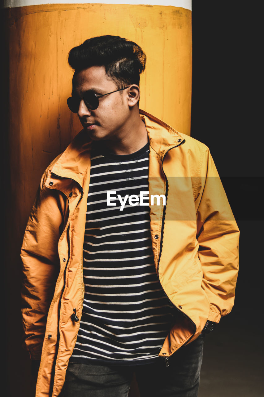 Young man wearing sunglasses standing against wall