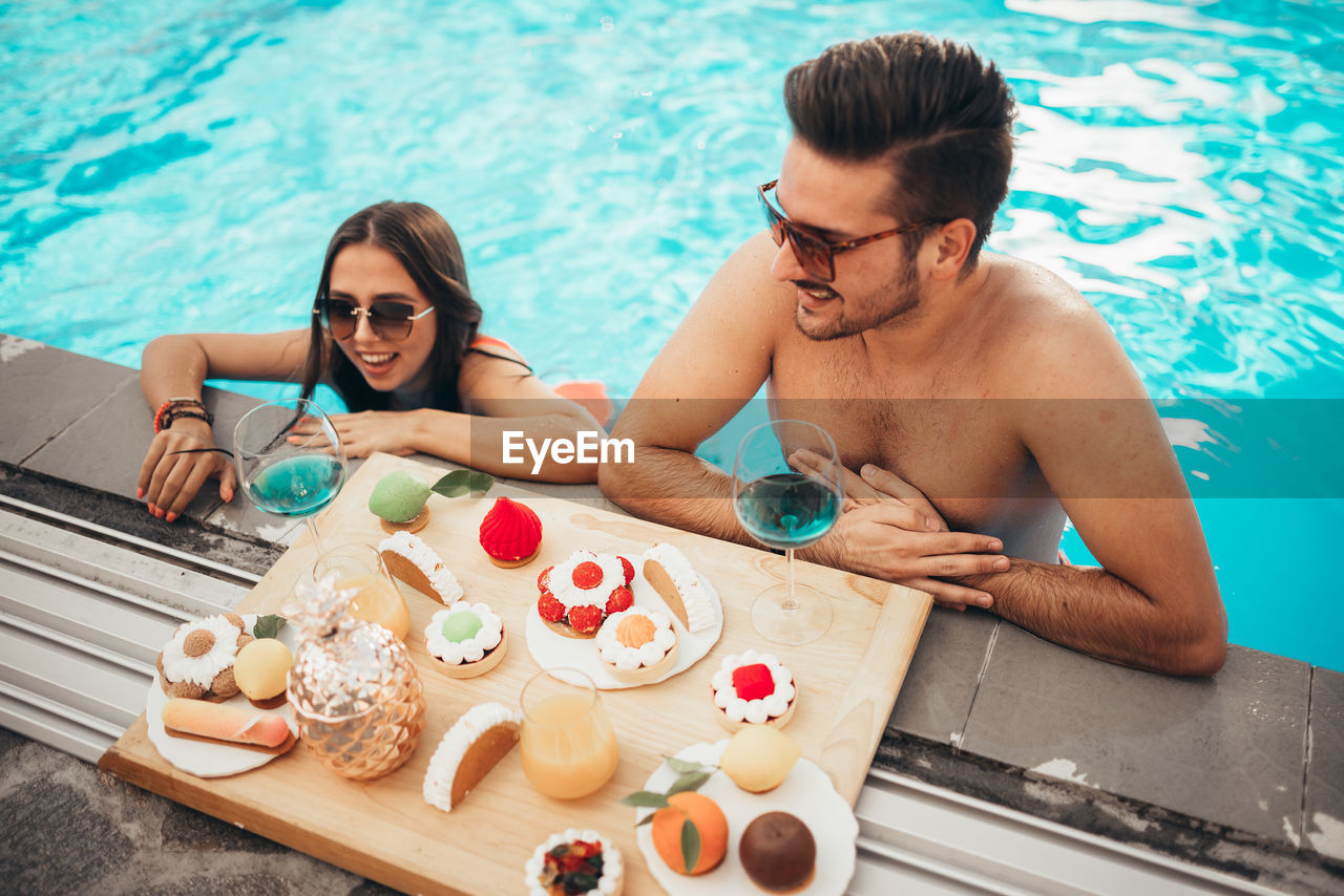 Beautiful couple enjoying tasty food in pool during tropical vacation