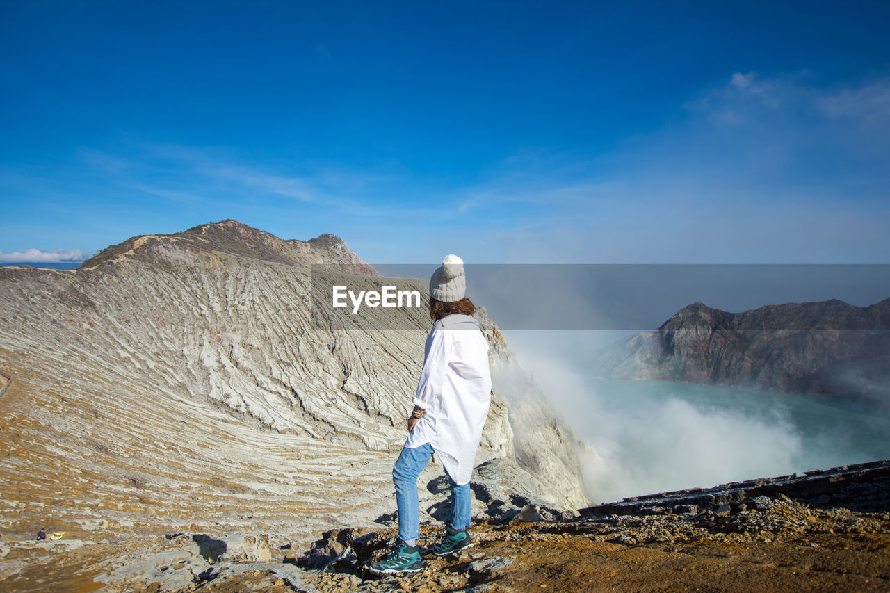 Woman looking at view of hot spring standing on mountain against sky