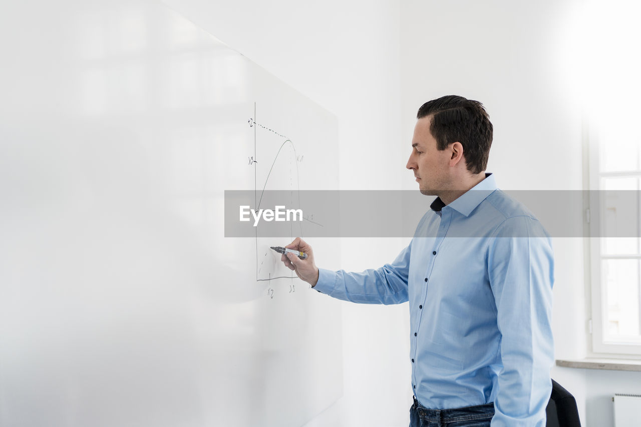 Businessman drawing chart on whiteboard at workplace