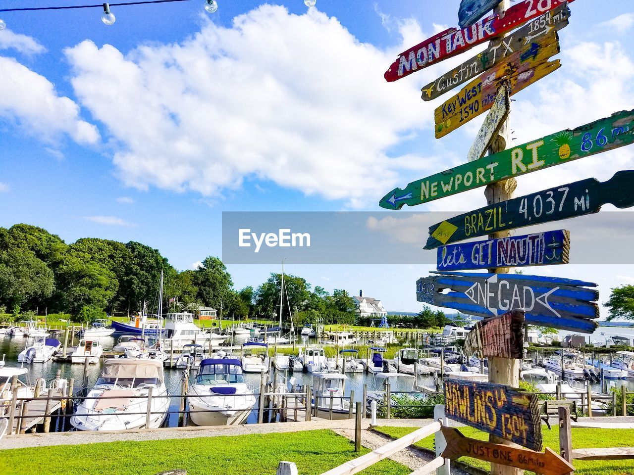 Marina sign with arrows pointing in the direction of cities against sky