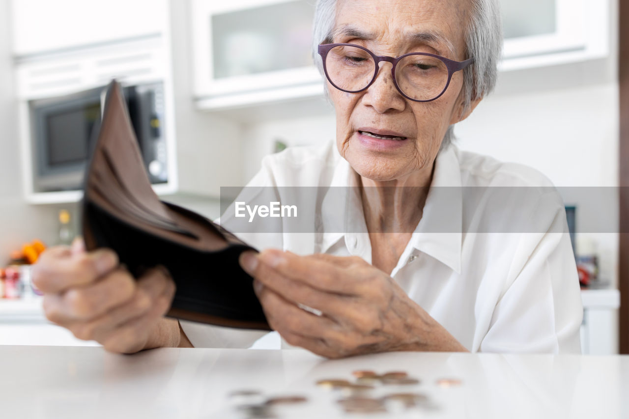 Close-up of senior woman removing coins from wallet on table