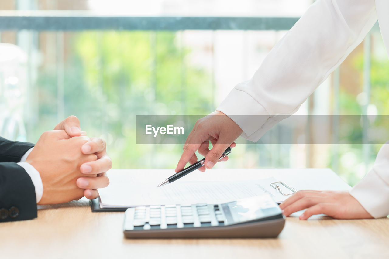 Midsection of woman showing contract paper to businessman on desk