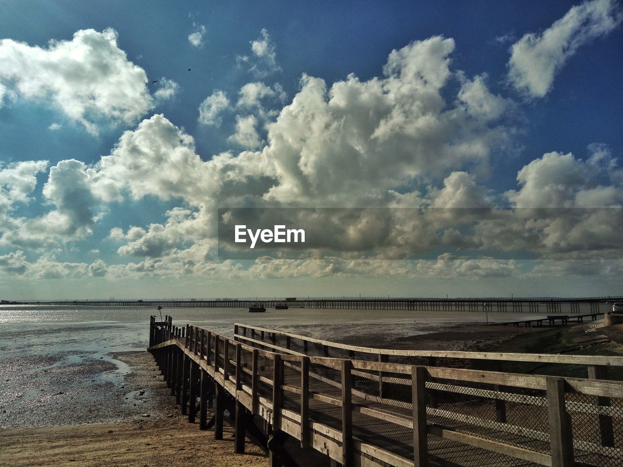 EMPTY JETTY LEADING TO CALM SEA AGAINST CLOUDY SKY