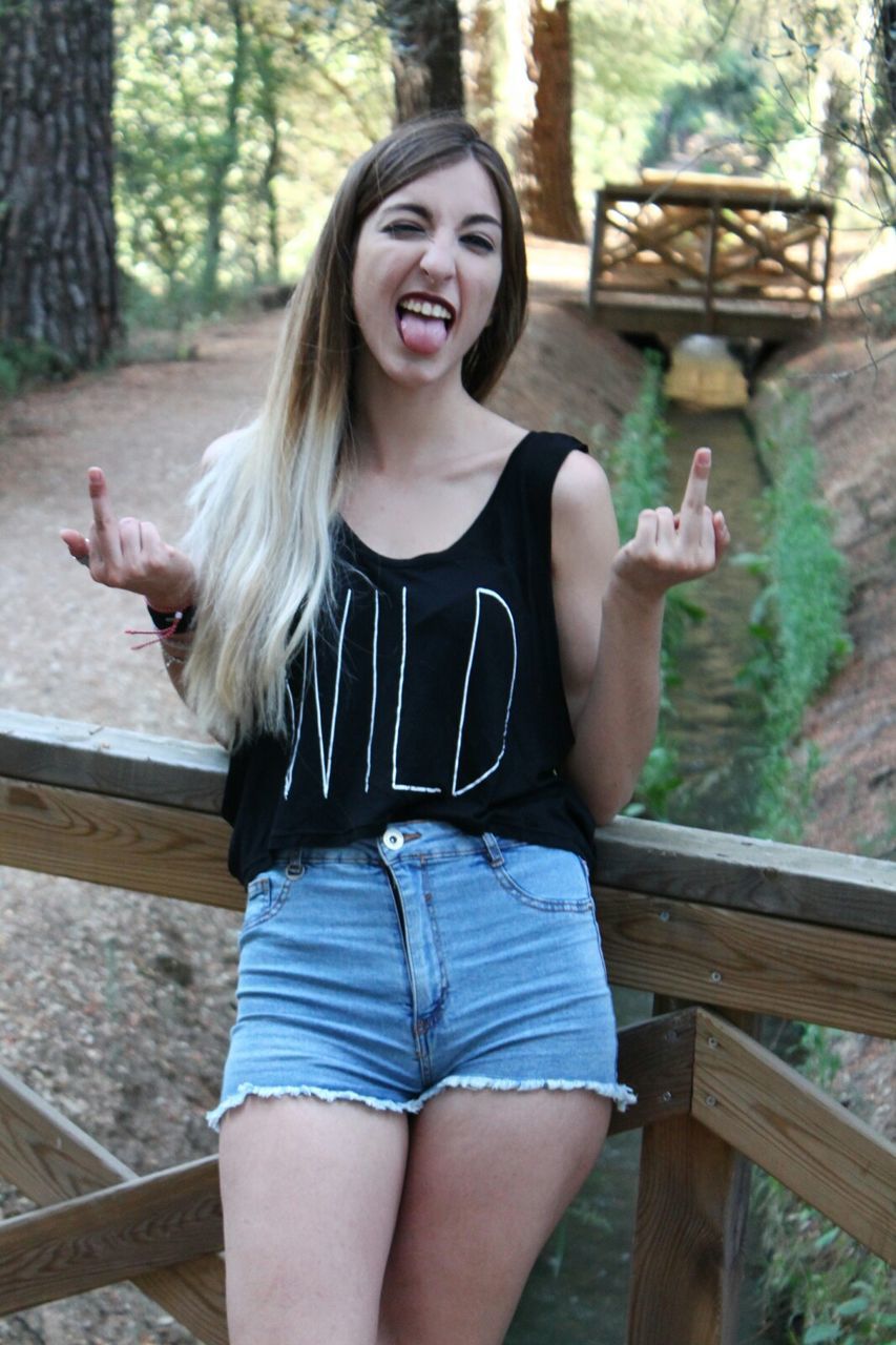 Young woman showing obscene gesture standing on bridge at forest