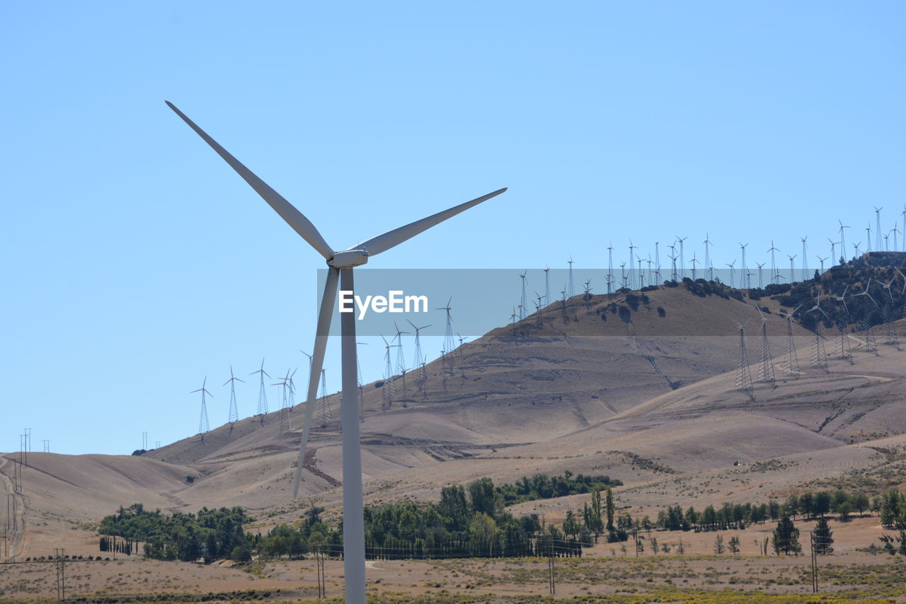 Windmills on landscape against clear sky