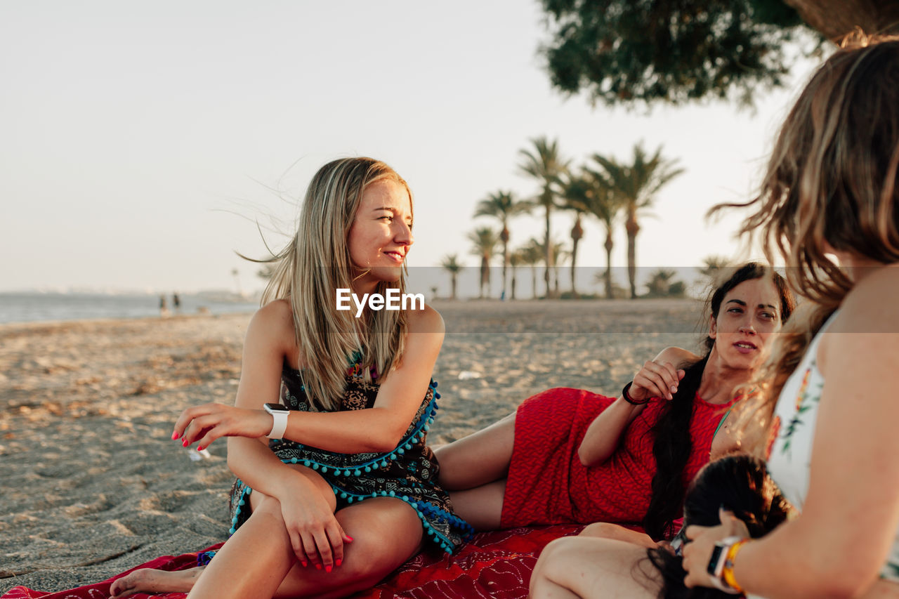 Female friends talking at beach against sky during sunset