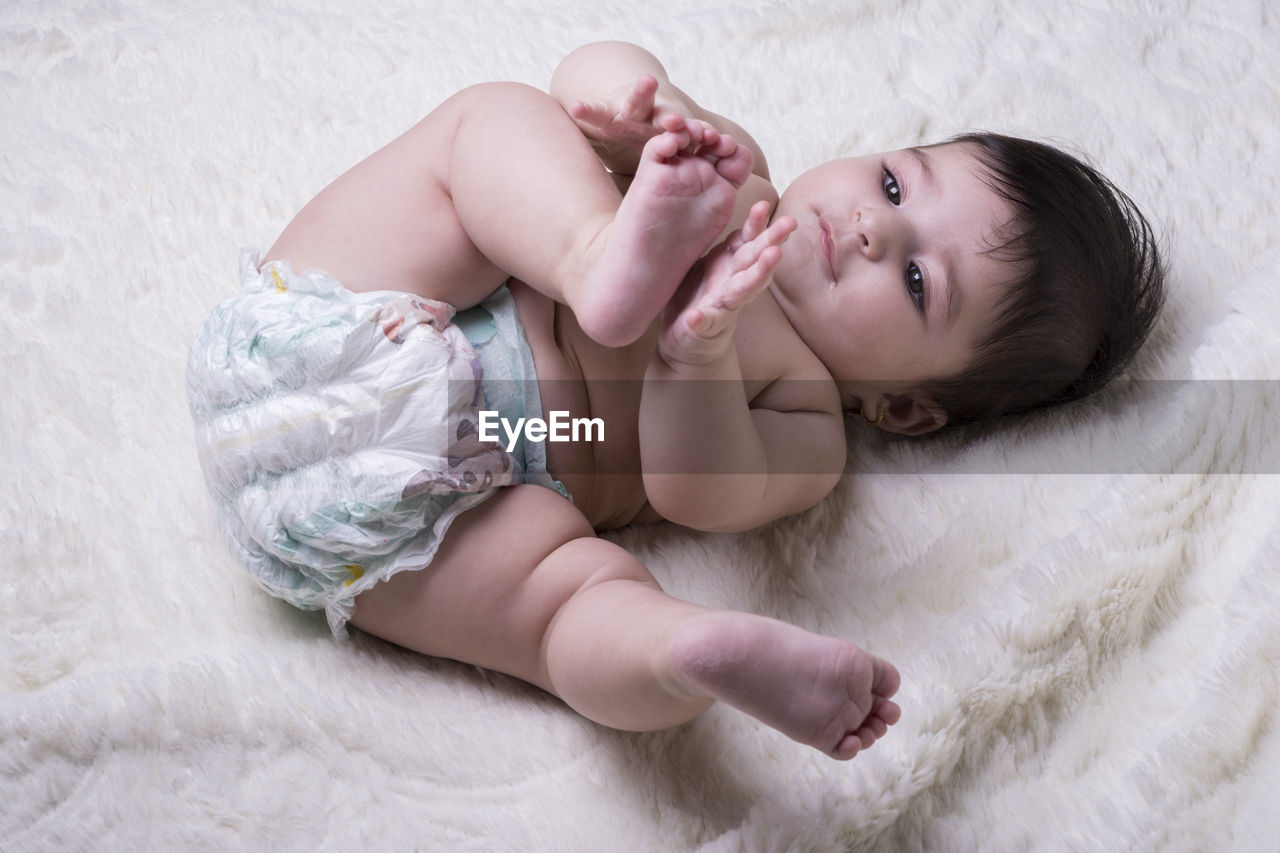 High angle view of shirtless baby girl lying on bed