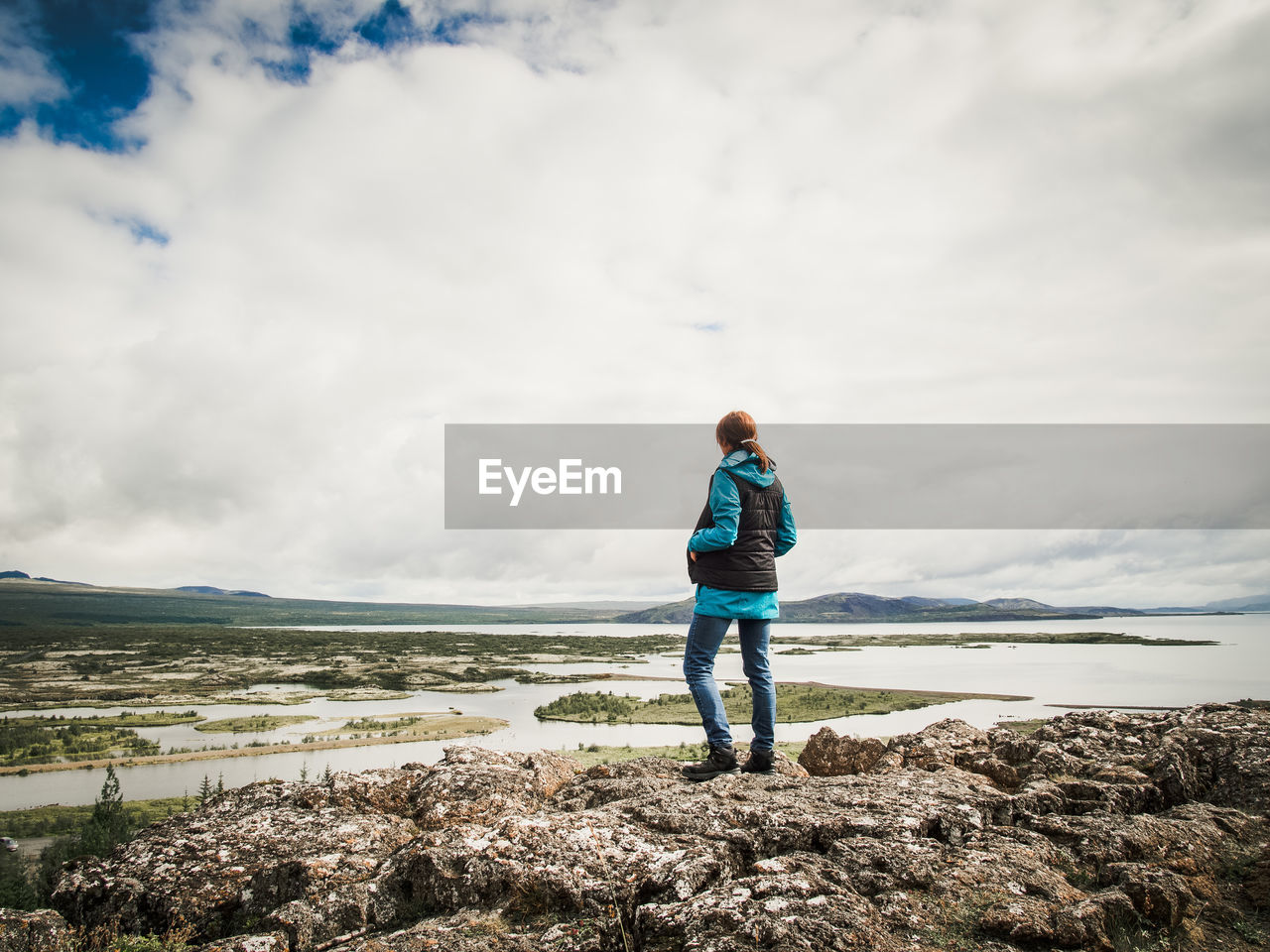 Rear view of woman standing on rock by sea against cloudy sky