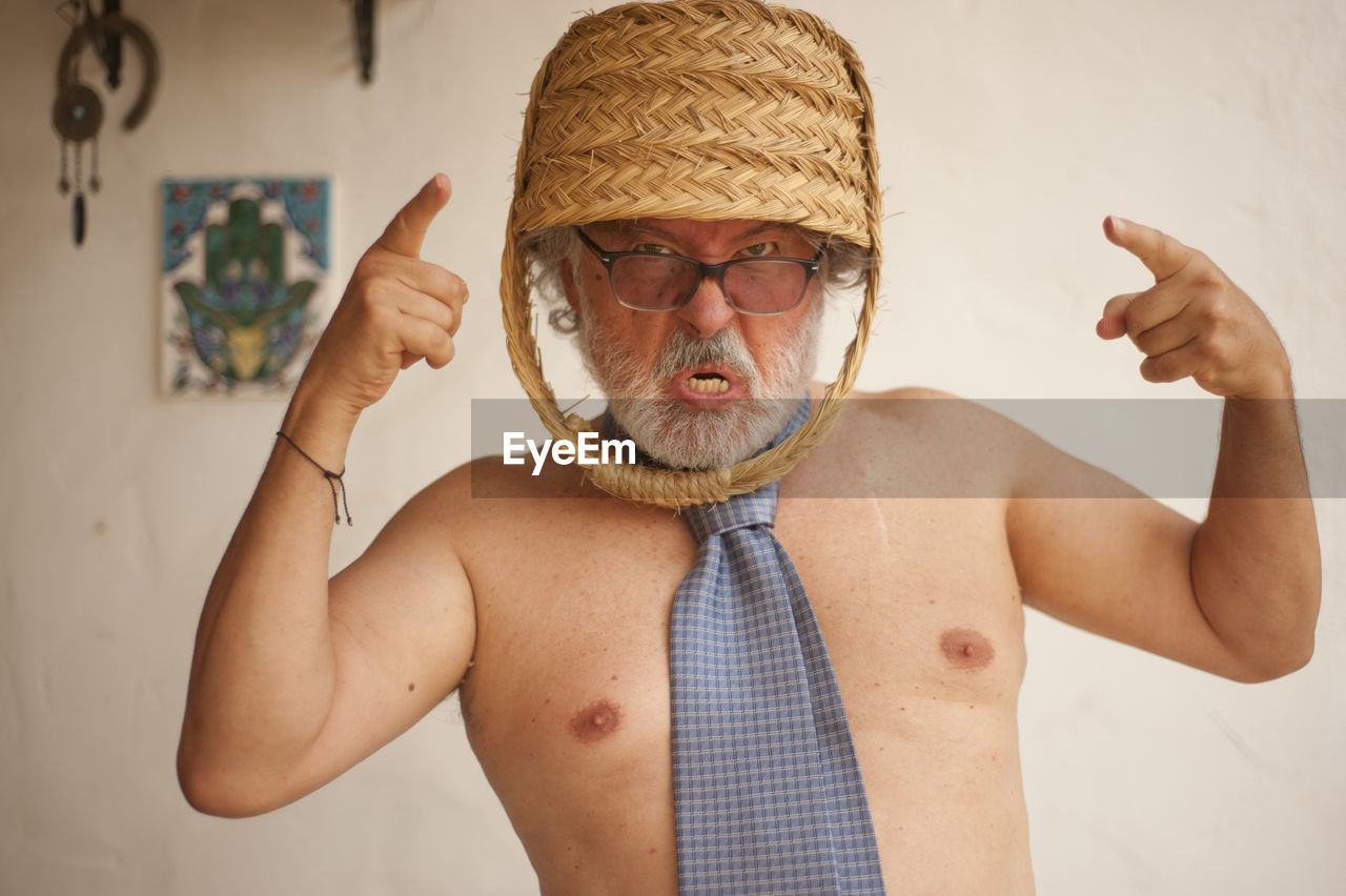 PORTRAIT OF SHIRTLESS MAN WITH ARMS RAISED STANDING IN FRONT OF HAT