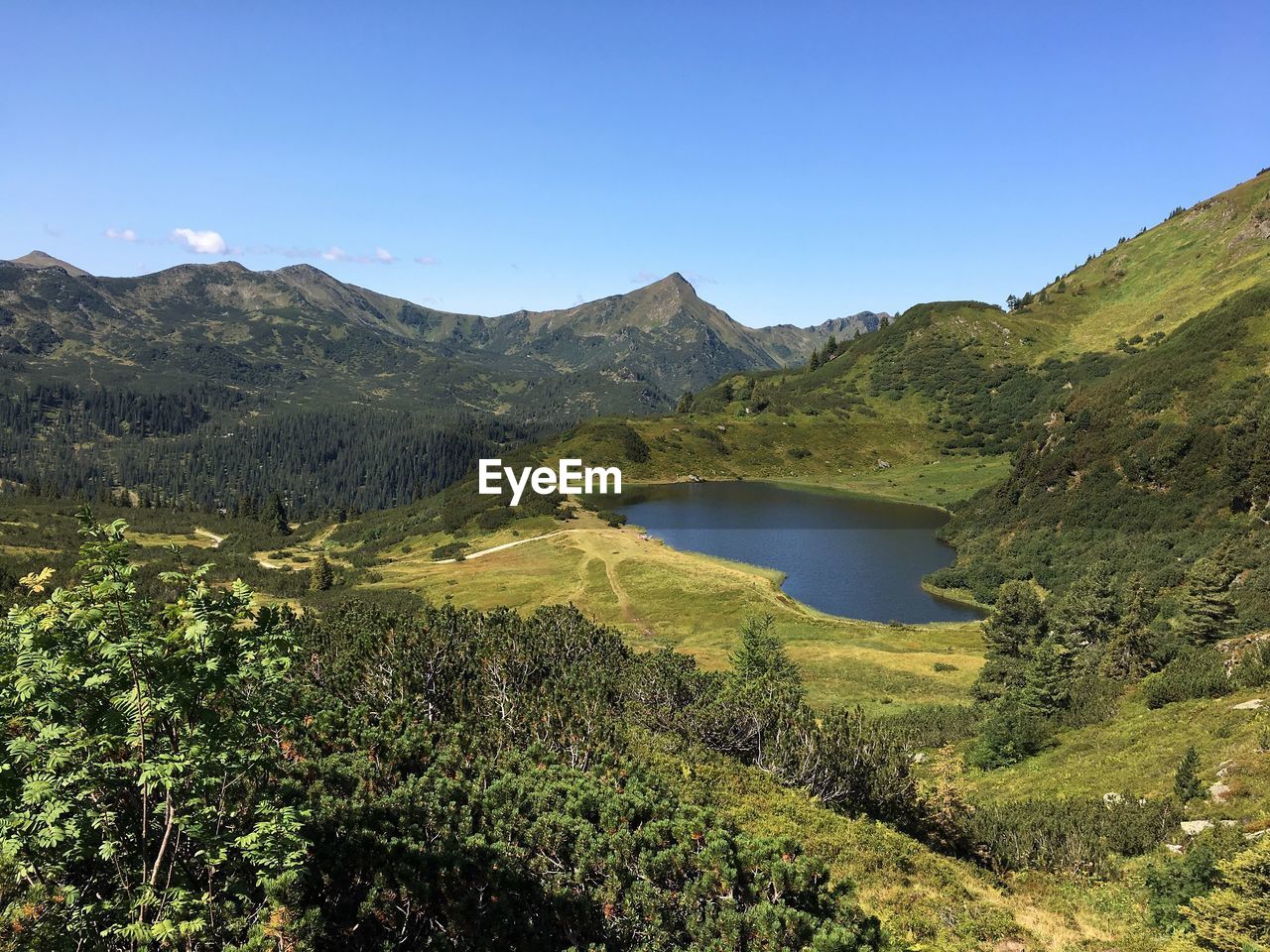 Scenic view of lake and mountains against clear blue sky