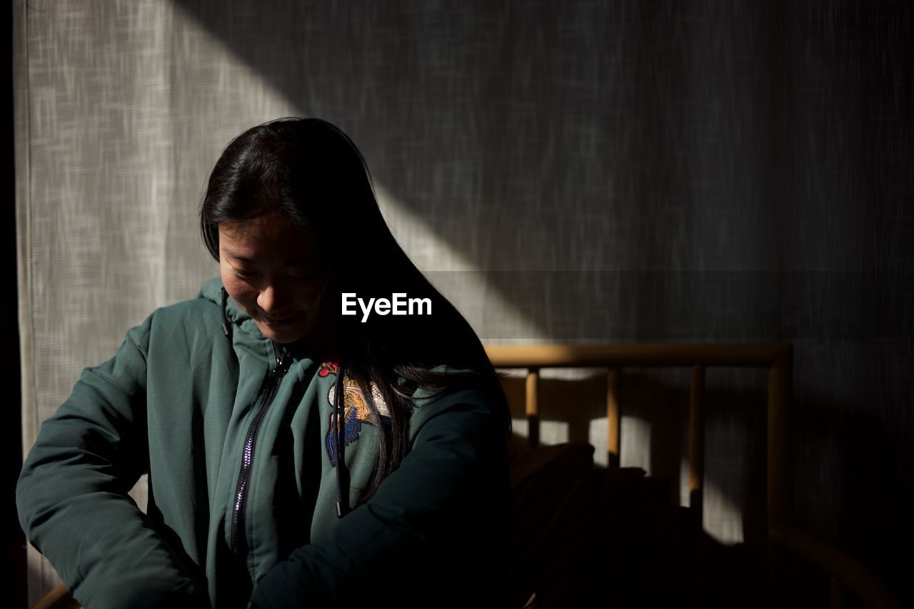 Woman wearing jacket while sitting against curtain at home