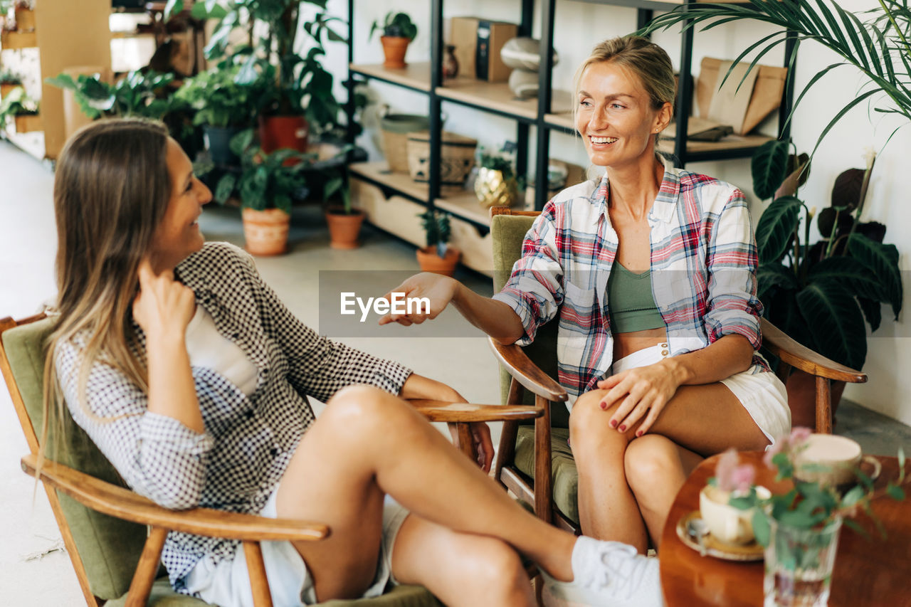 Two young attractive women are chatting while sitting in a cafe.