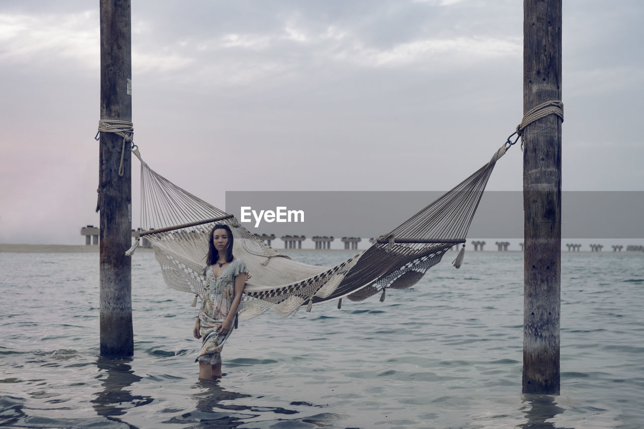 Woman standing in sea against hammock