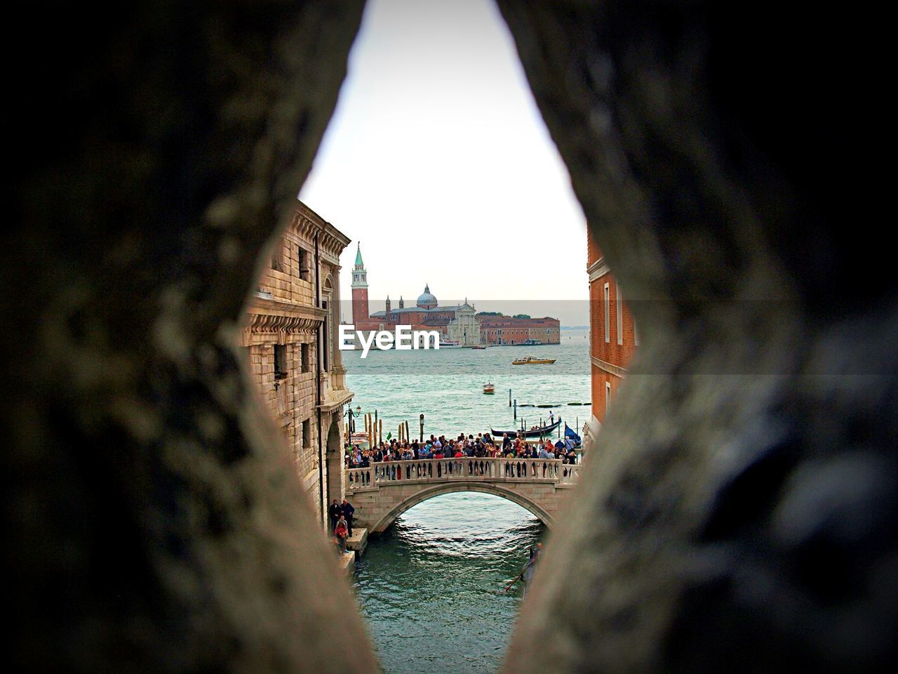 People on bridge over river against palace seen from hole in wall