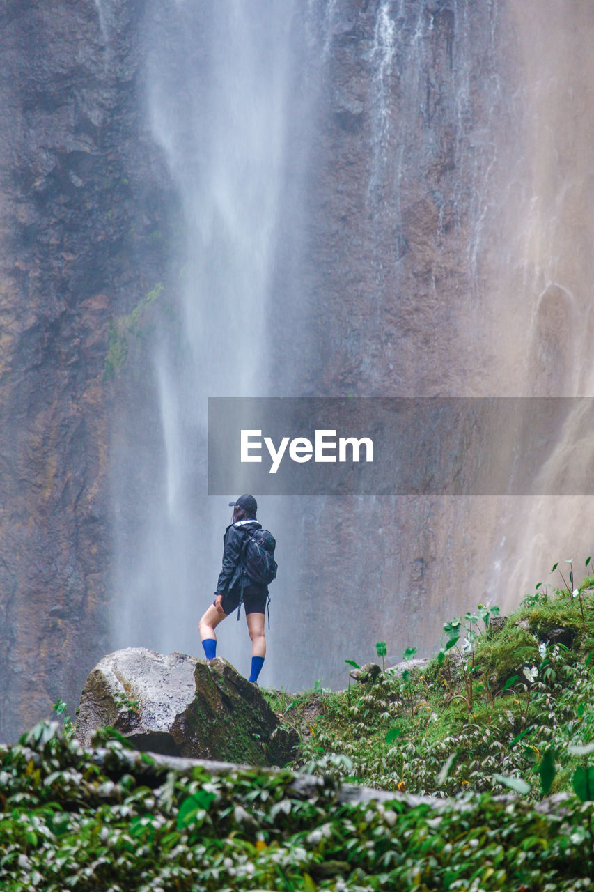 MAN STANDING AGAINST WATERFALL