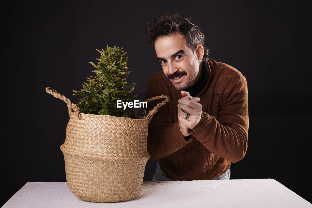 one person, adult, men, person, indoors, studio shot, black background, portrait, plant, beard, facial hair, clothing, picnic basket, container, basket, business, nature, holding, copy space, lifestyles, business finance and industry, young adult, front view, looking, flowerpot, emotion, food and drink