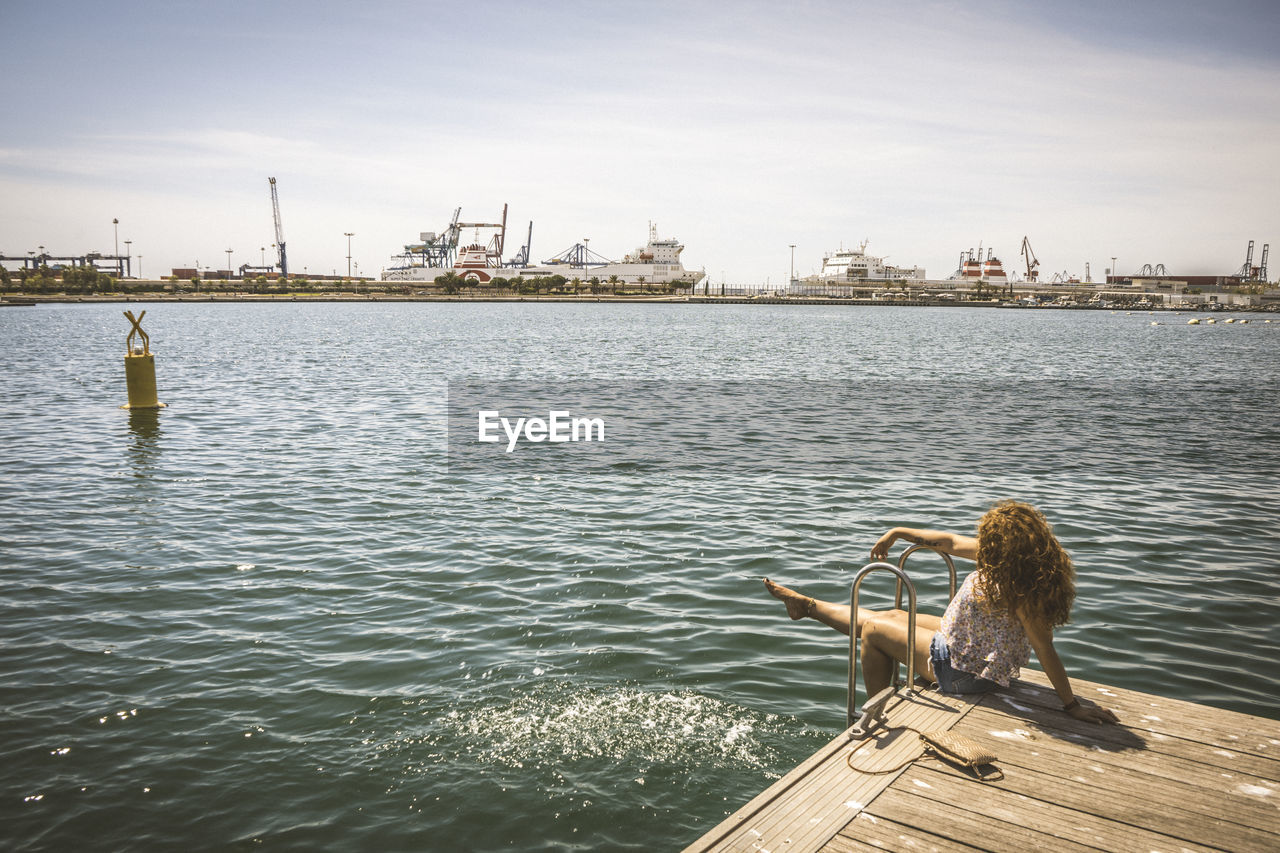 Woman sitting on pier over sea against sky
