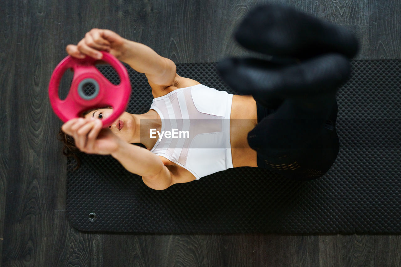 High angle view of woman holding equipment while exercising on floor