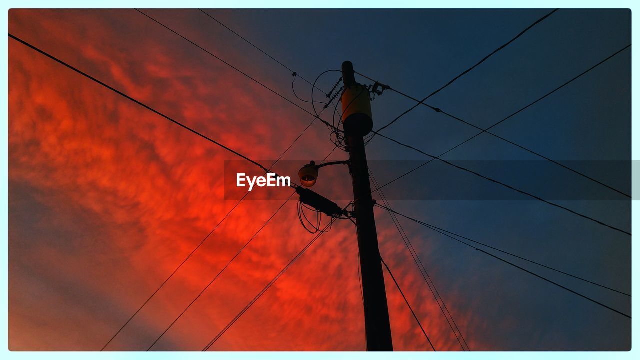 Low angle view of electricity pylon against sky during sunset