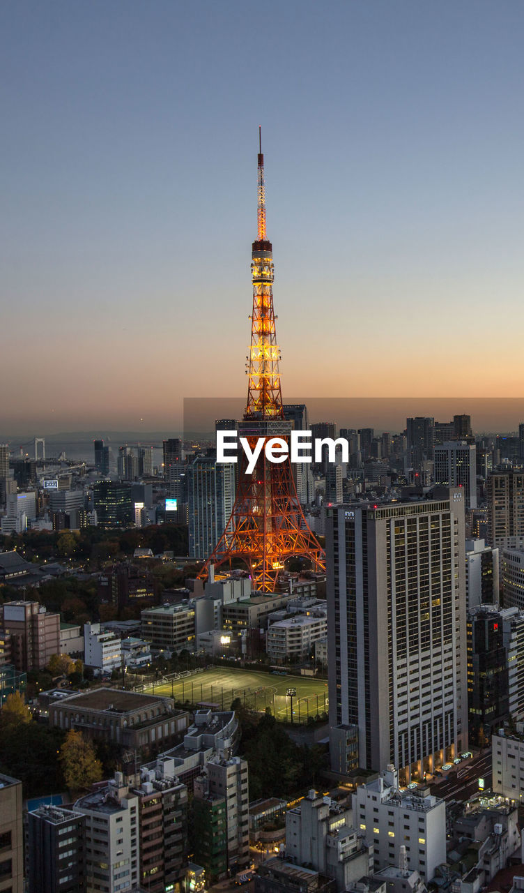 Illuminated tokyo tower in city against clear sky during sunset