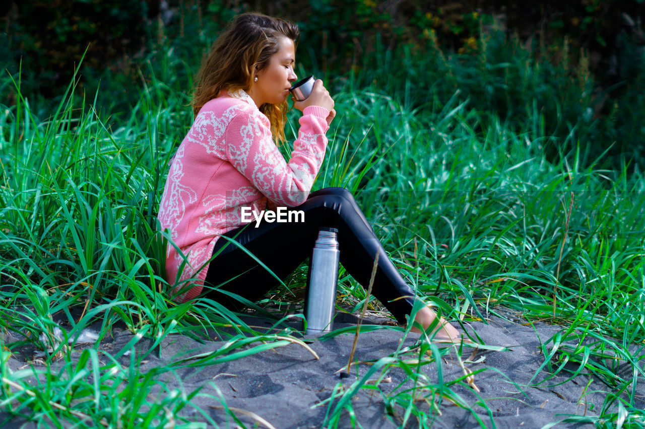 Full length of woman drinking water while sitting on grass