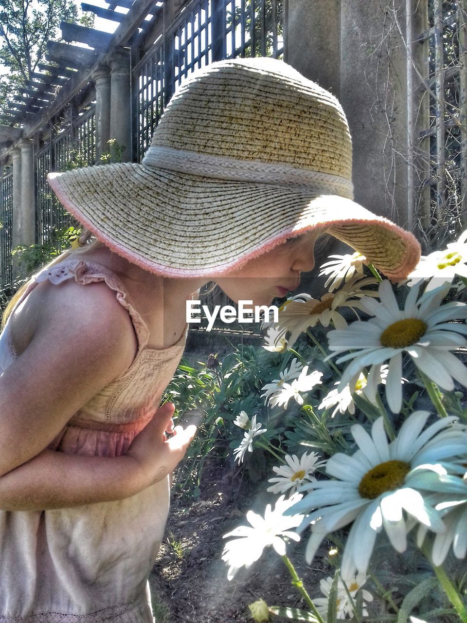 Side view of girl wearing hat kissing flower at park