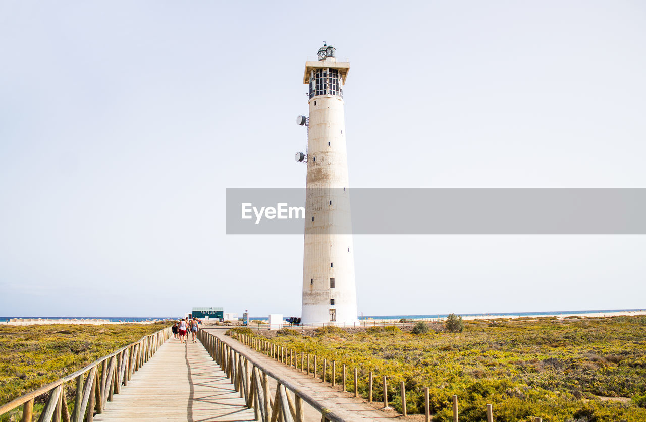 People walking on road by lighthouse against clear sky