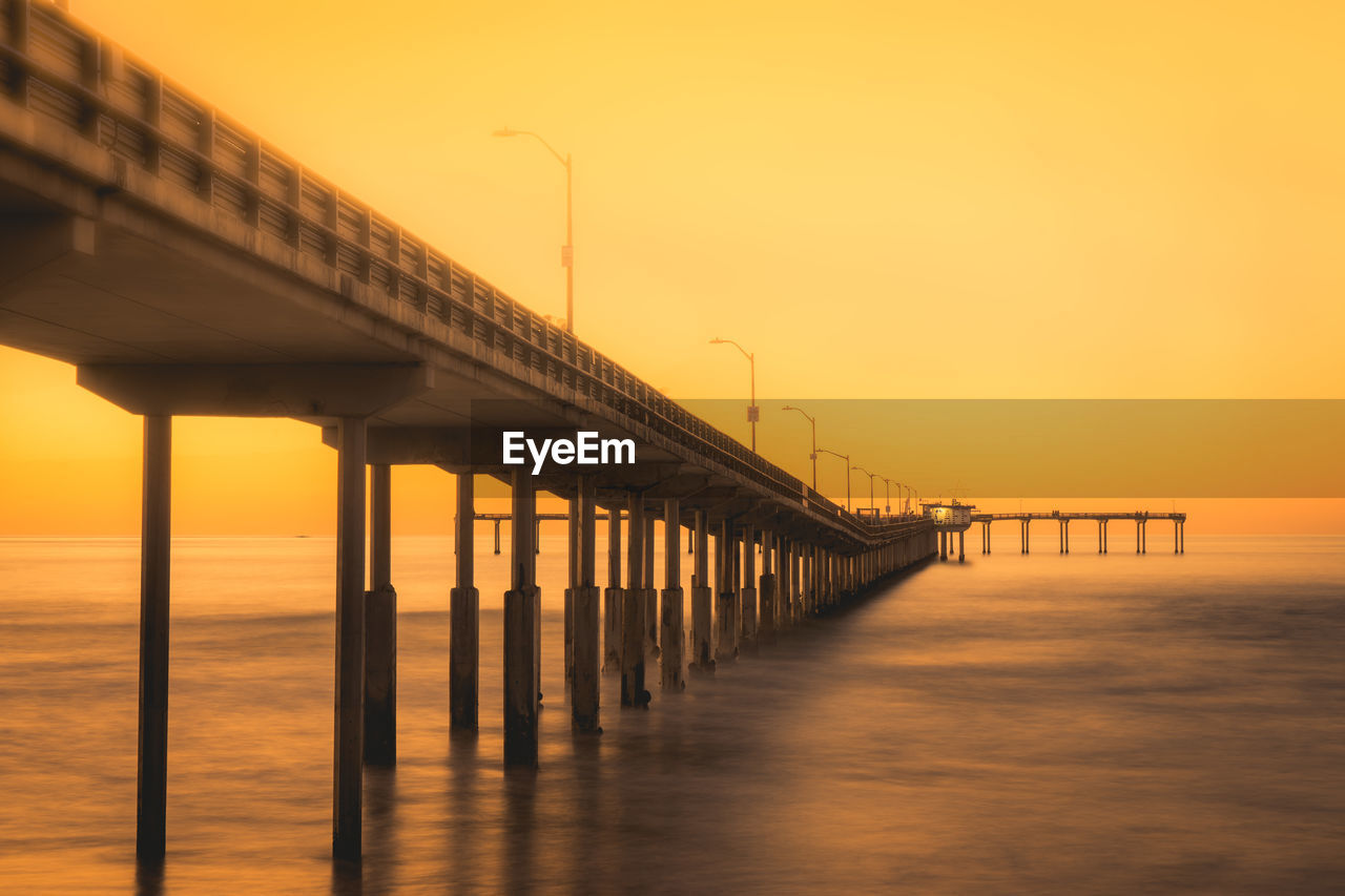 Pier over sea against orange sky