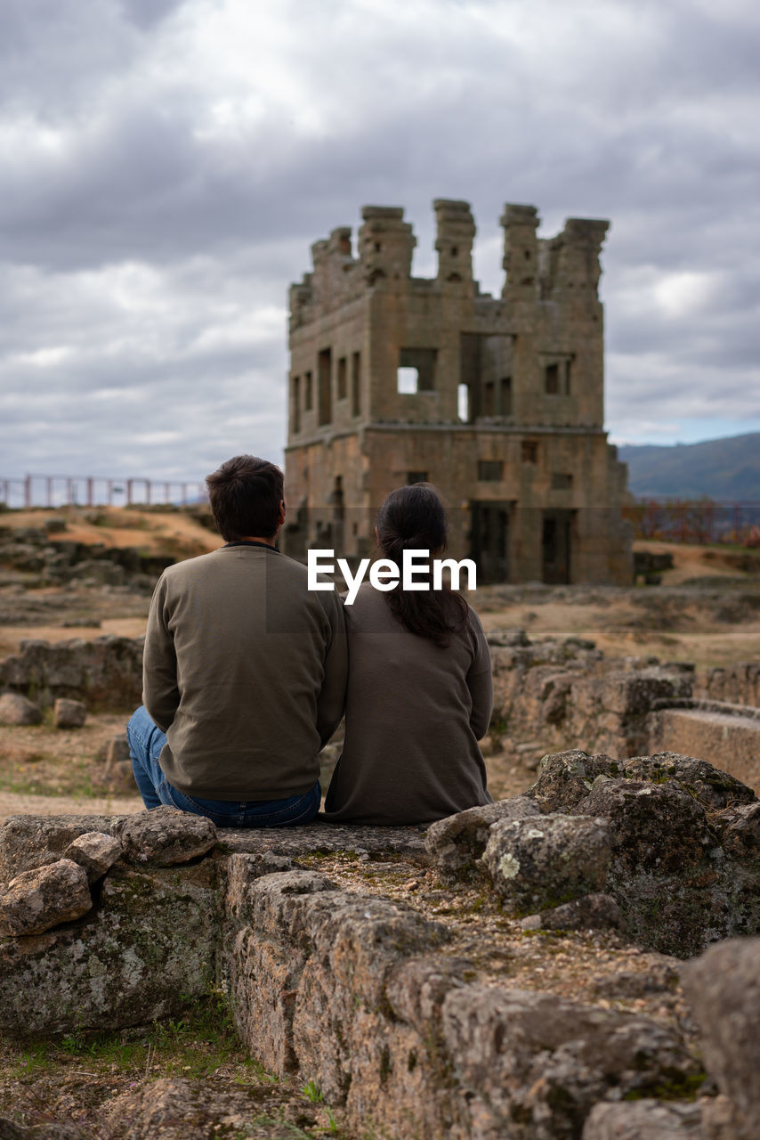 Rear view of men sitting on stone wall