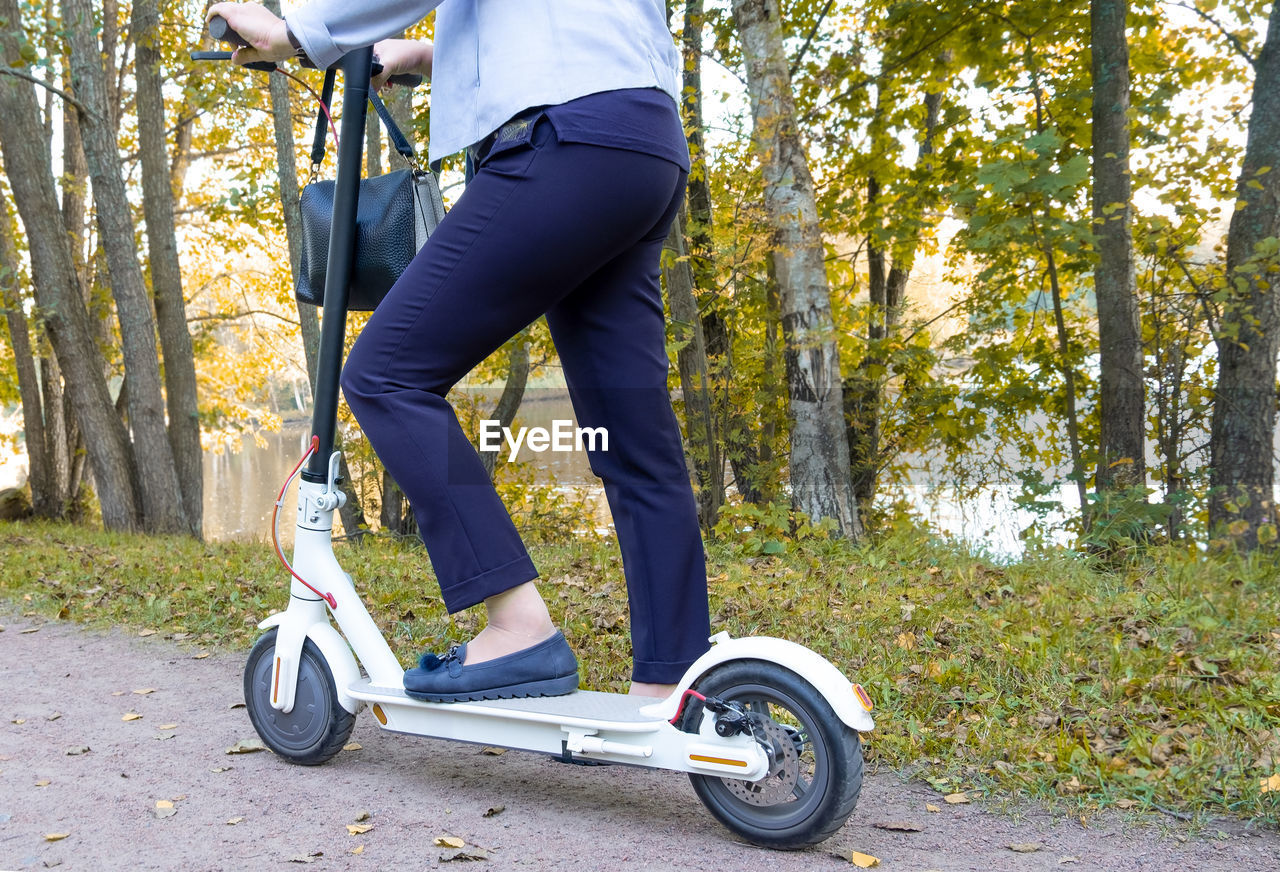 An adult elegant woman is about to ride an electric scooter in the park in early fall. 