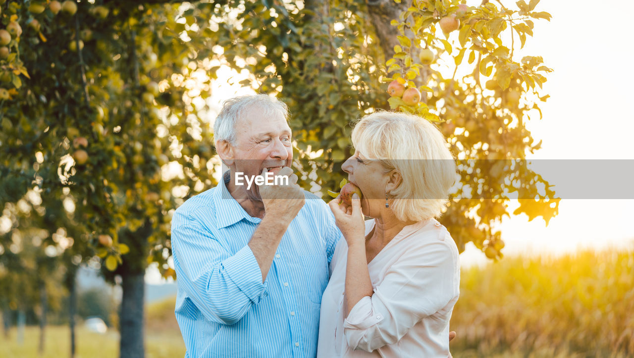 Senior couple eating apple while standing outdoors