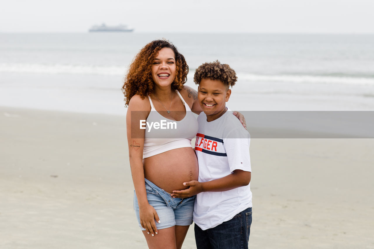 Brother posing with pregnant sister on beach