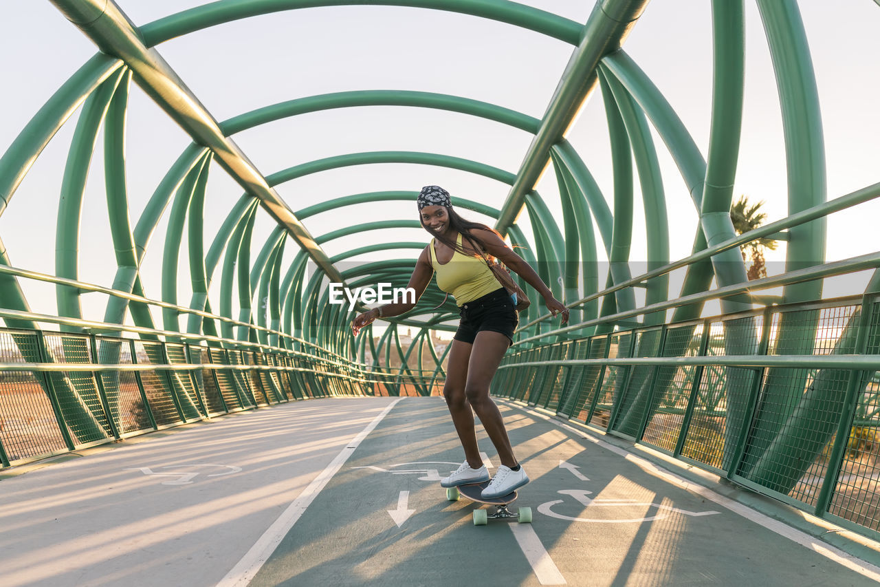 Smiling mid adult woman skateboarding on bridge