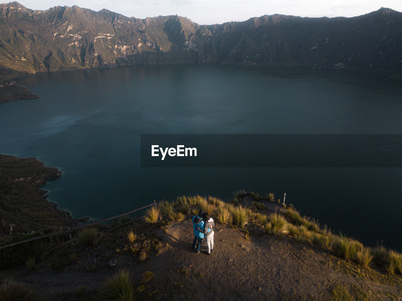 Couple standing in the mountains with lake behind drone view