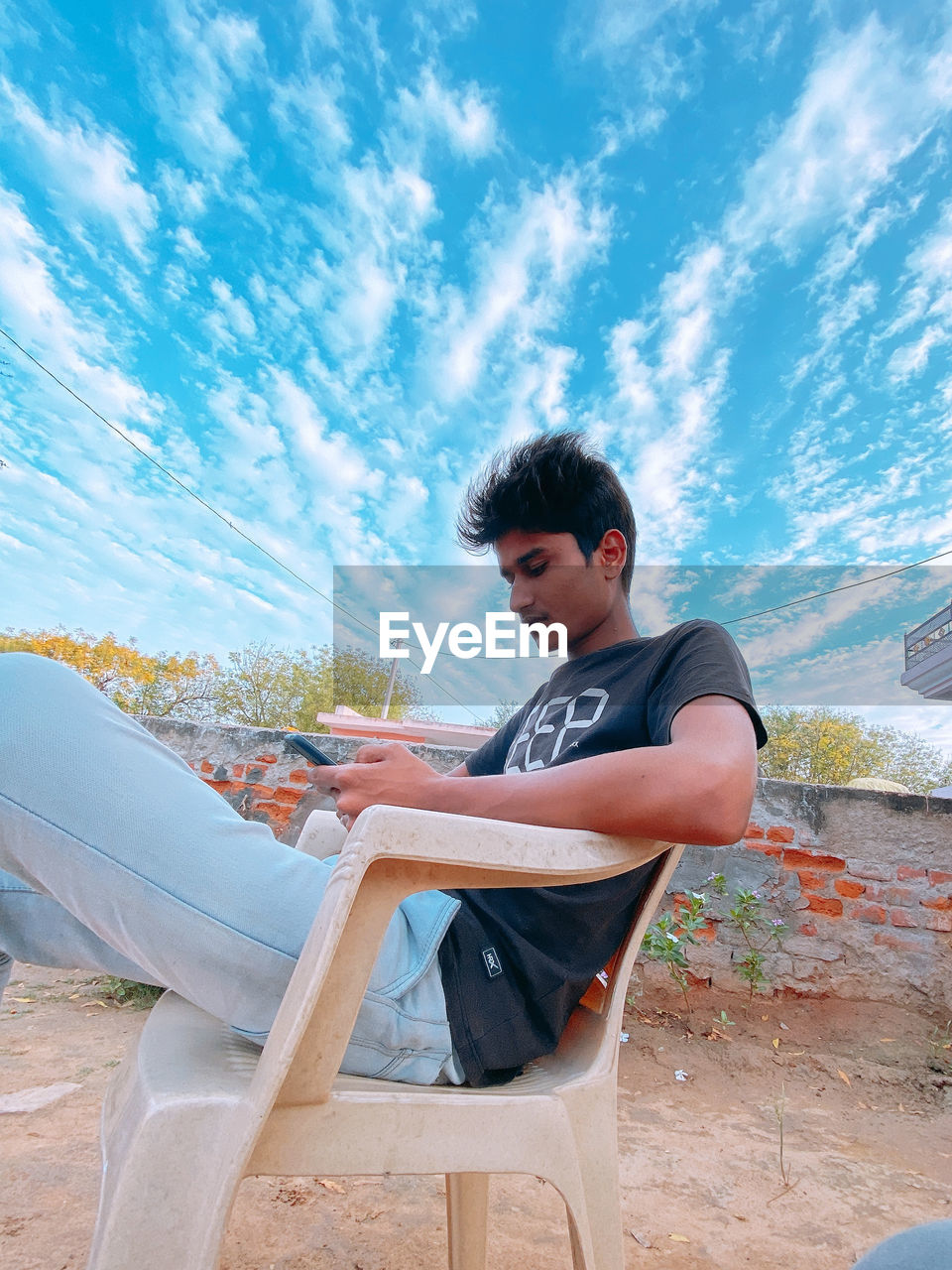 Young man sitting on seat against sky