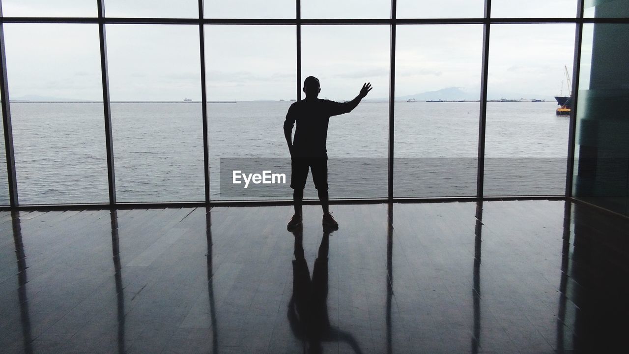 Silhouette man looking at sea through window