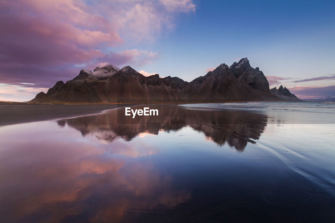 Scenic view of mountain reflected on wet beach during sunset