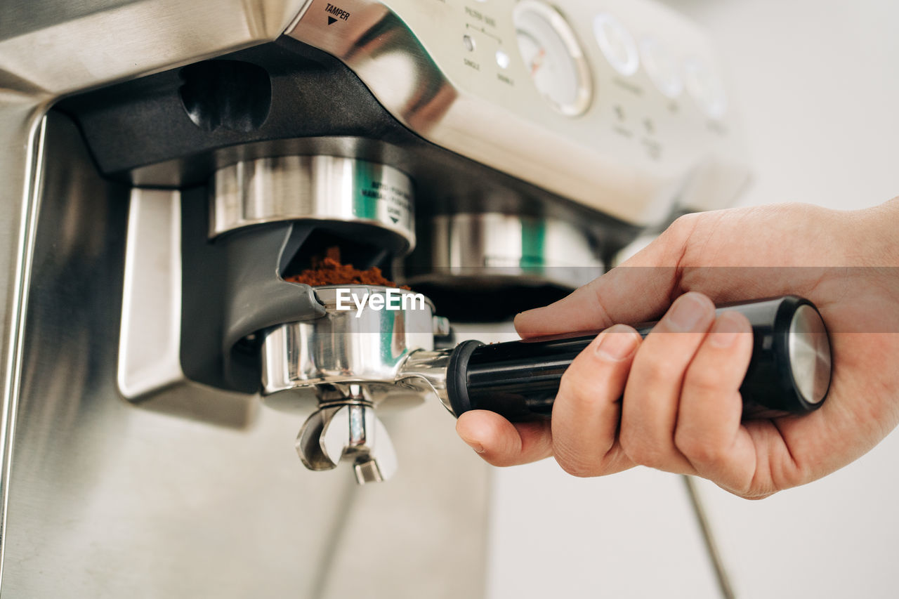 Crop unrecognizable person inserting portafilter with ground coffee into modern espresso maker in house person