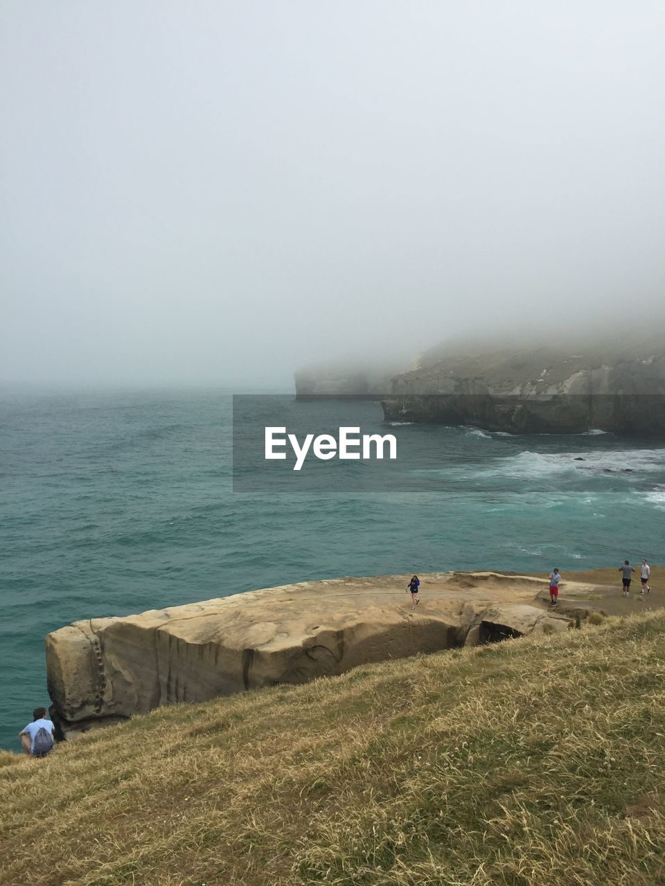 Tourists on cliff by sea at tunnel beach during foggy weather
