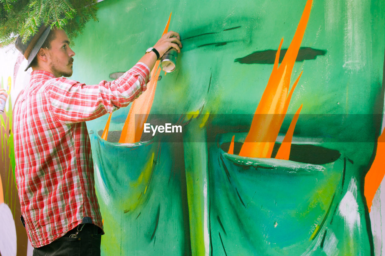 Young man spray painting graffiti on surrounding wall