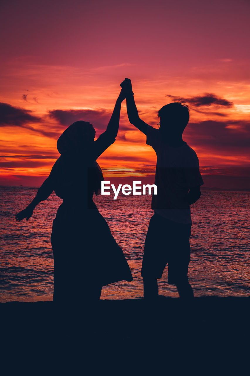 SILHOUETTE WOMEN STANDING ON BEACH AGAINST ORANGE SKY