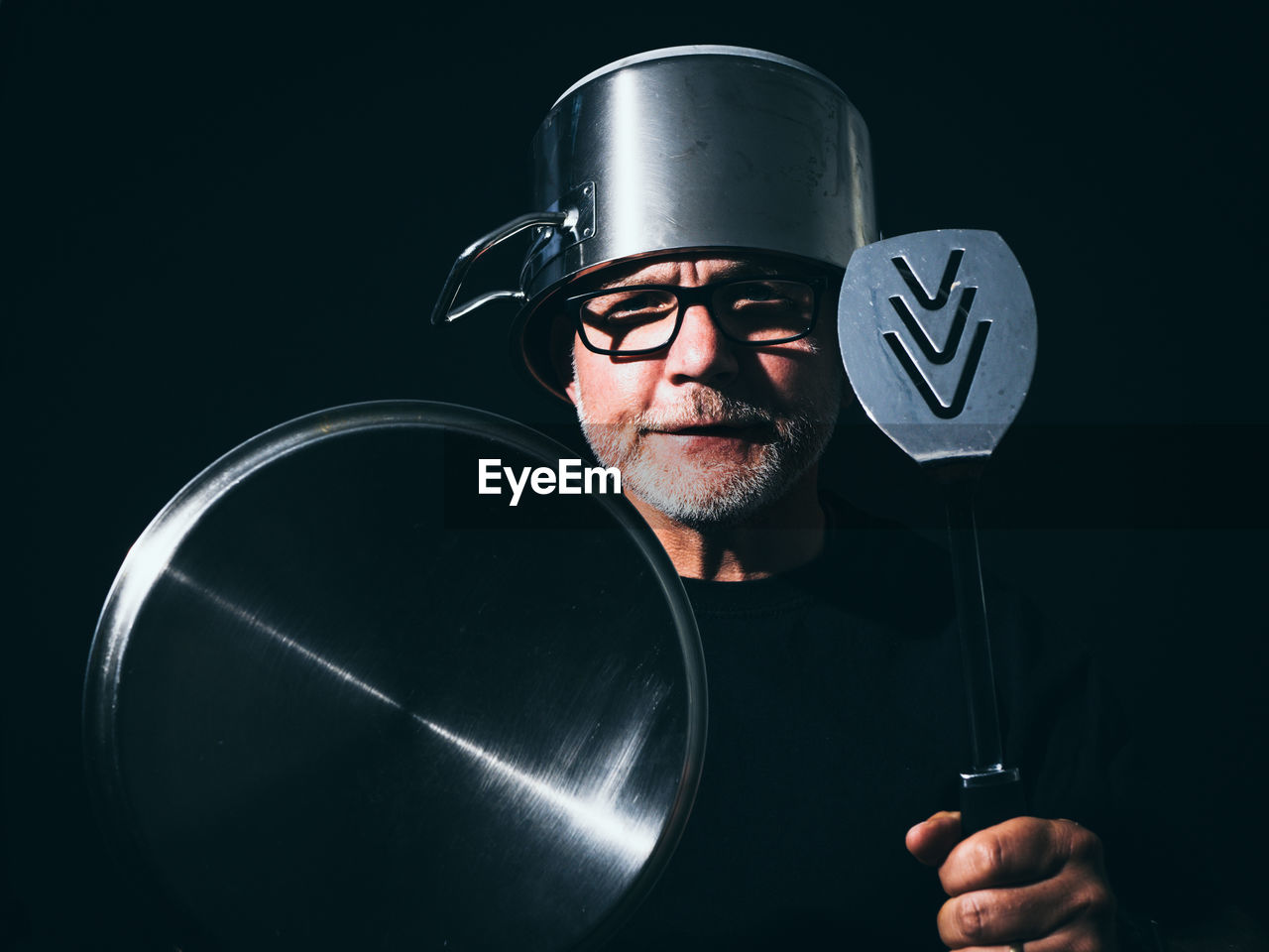 Portrait of man with kitchen utensils against black background